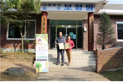 보령육아원 앞에서 봉사단 단장과 보령육아원 원장이 자매결연협약을 맺은 서류를 들고 찍은 사진
